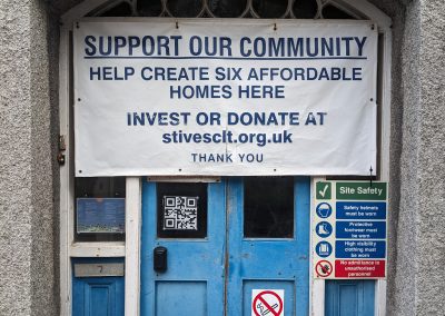 An image of St Ives CLT's Old Vicarage's front door. There is a banner on it reading "Support our communit - help create 6 affordable homes here. Invest or donate at Stivesclt.org.uk Thank you"