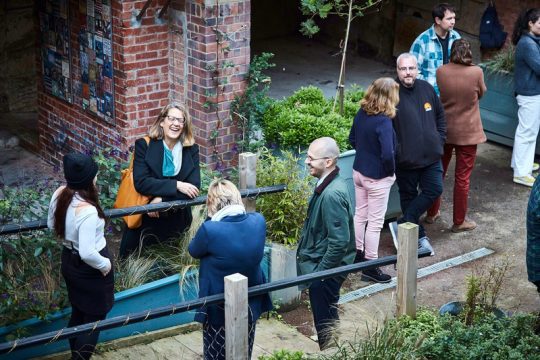 Image shows groups of people talking and laughing standing in an alley by a Hastings Commons project
