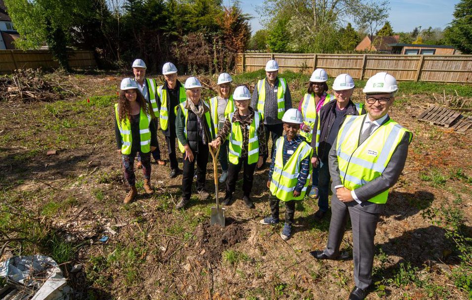 A family of four and their dog sitting in their new home around the table with their hands touching in the middle of the table
